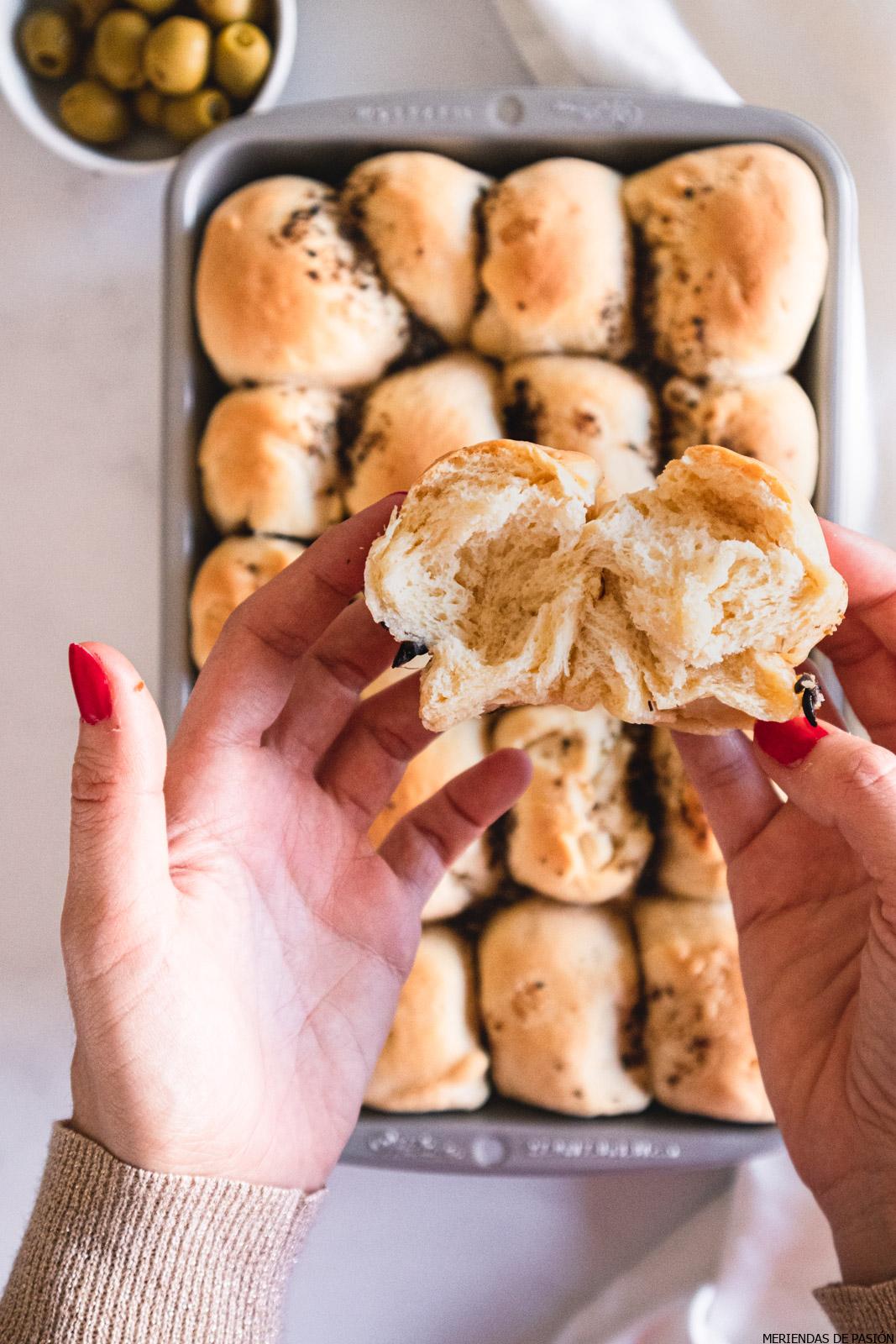 Olive butter dinner rolls being opened by a woman's hands.