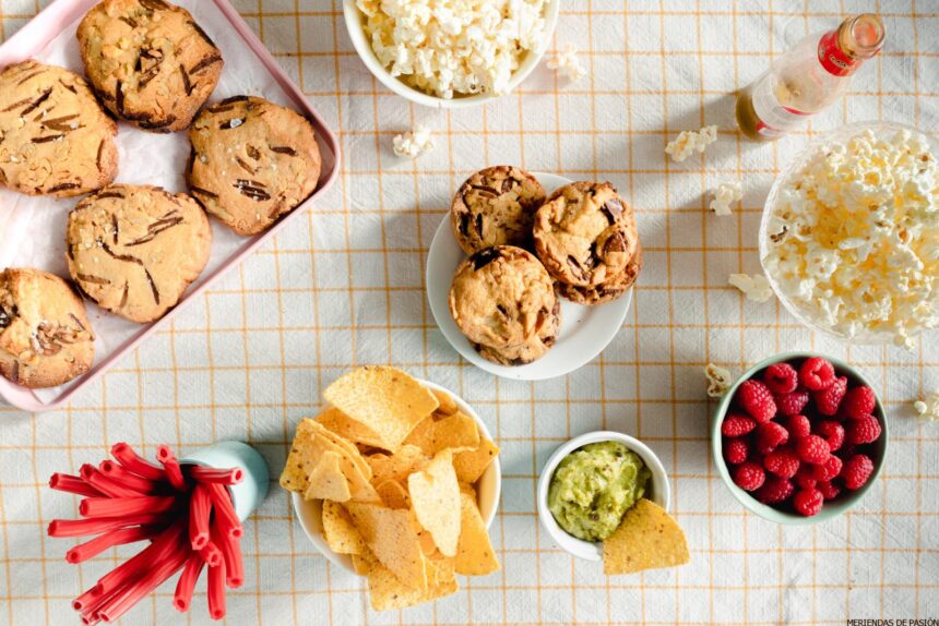 Una mesa llena de cookies, papas fritas y un tazón de guacamole.