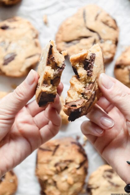 Dos manos sosteniendo una galleta con trocitos de chocolate con un bocado sacado de ella.