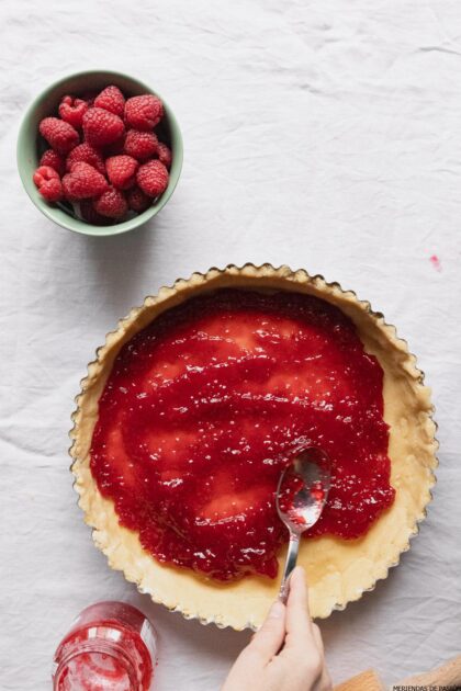 Una persona que vierte salsa de frambuesa en un molde para tarta.