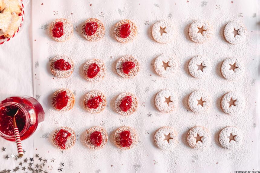 Galletas navideñas con mermelada de frambuesa sobre un mantel blanco.