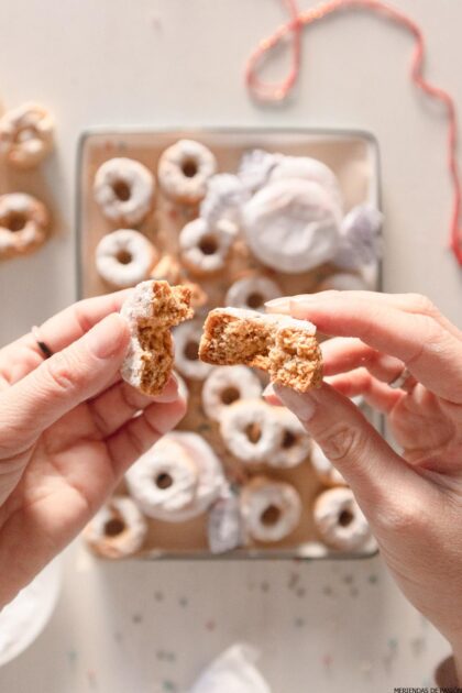 Una persona sostiene un trozo de donut frente a una bandeja.