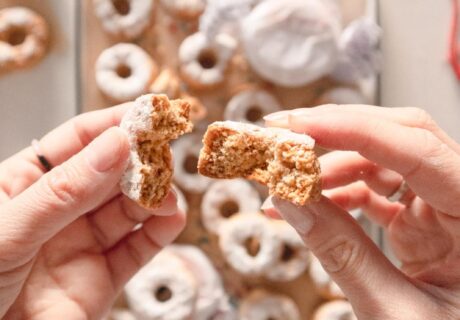 Una persona sostiene un trozo de donut frente a una bandeja.