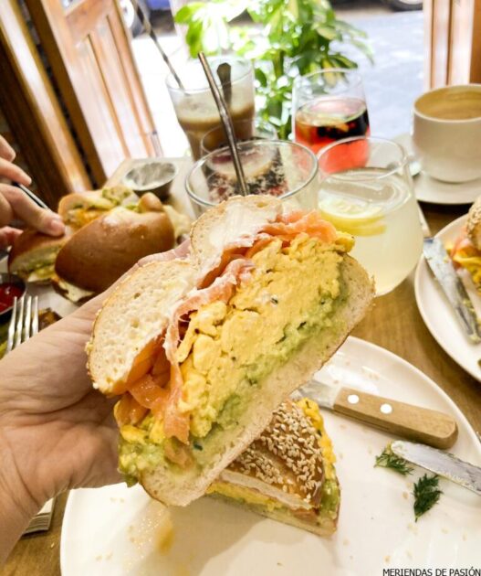 Una persona sostiene un sándwich sobre una mesa.