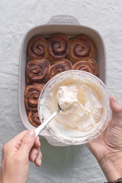 Una persona vierte crema en una sartén con panecillos de canela.