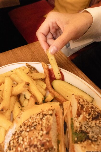 Una persona comiendo un sándwich y papas fritas en un plato.