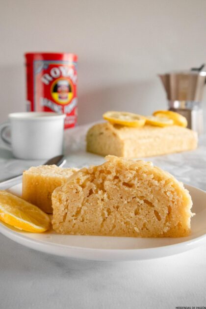 Un trozo de tarta de limón en un plato junto a una taza de café.