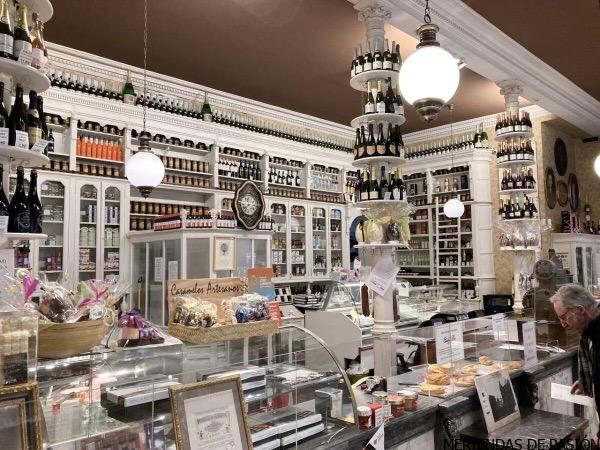 Una delicatessen antigua con una variedad de productos en exhibición, atendida por un empleado mientras los clientes curiosean.