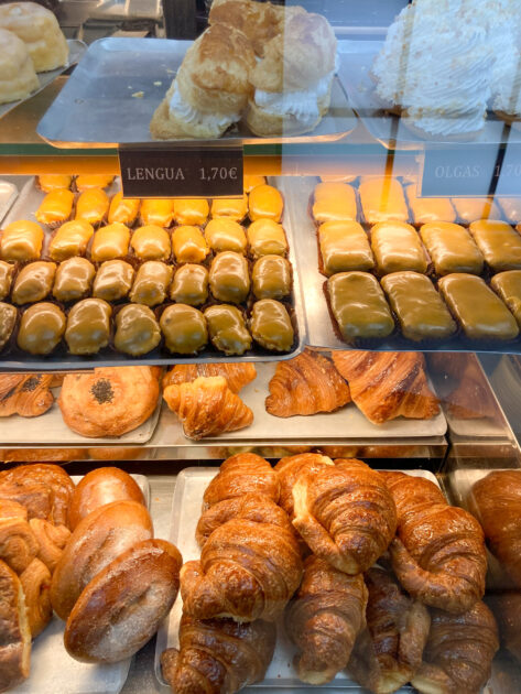 Una vitrina llena de pasteles variados, incluidos croissants y bollos glaseados, con etiquetas de precios en euros.