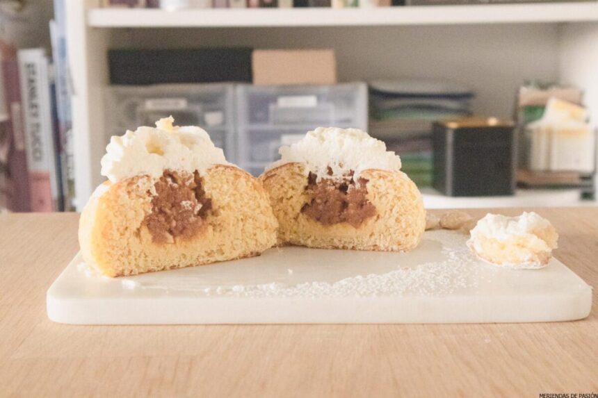Dos pasteles rellenos de crema abiertos y espolvoreados con azúcar en polvo sobre una tabla de cortar.