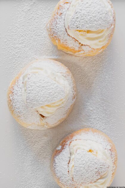 Tres pasteles rellenos de crema espolvoreados con azúcar en polvo sobre una superficie blanca.