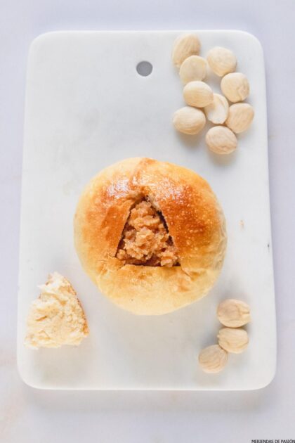 Un semlor sin nata, sobre una tabla de mármol con unas almendras al lado.