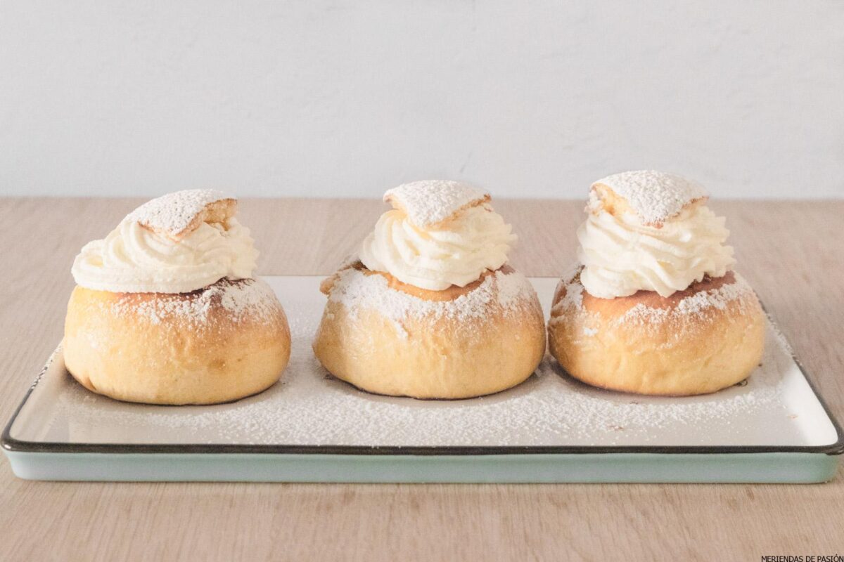 Tres pasteles rellenos de crema espolvoreados con azúcar en polvo en un plato.