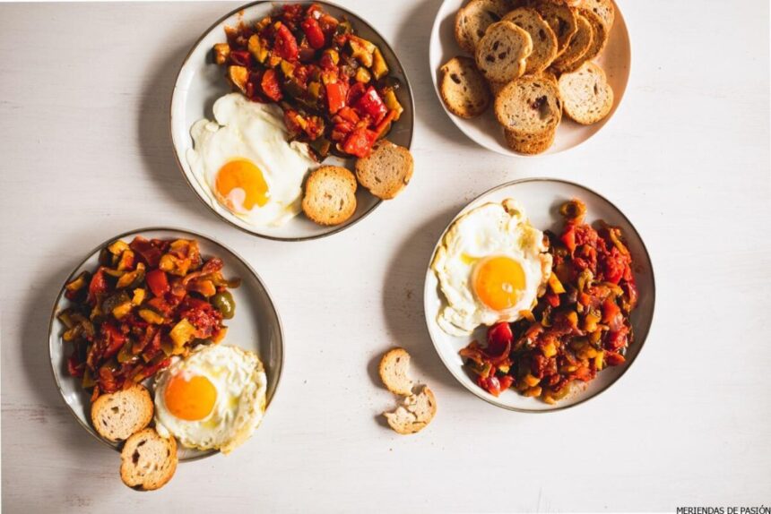 Tres platos con huevos fritos, pisto y rebanadas de pan tostado dispuestos sobre una superficie de madera clara.