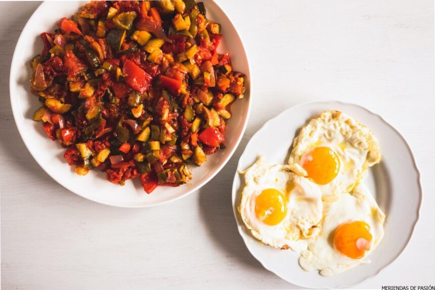 A plate of pisto next to a plate with three sunny-side-up eggs on a white table.