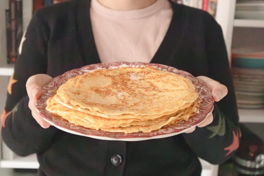 Una persona que sostiene un plato lleno de varios frixuelos asturianos, de pie en el interior con estantes de platos en el fondo.