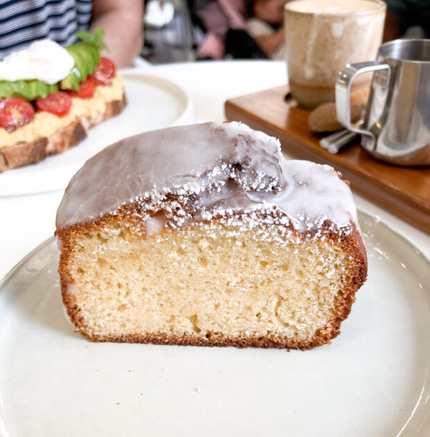 Una rebanada de bizcocho cubierto de frosting en un plato blanco con una taza de café.
